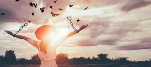 Woman facing sunshine breaking free from chains with birds flying — symbol of freedom and empowerment for burnt-out mums